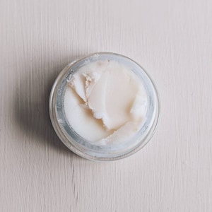 May include: A small glass jar with a white lid containing a white, creamy substance.