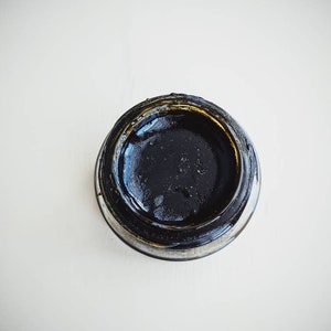 May include: A small glass jar with a black lid filled with a dark, viscous liquid.