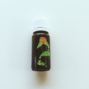 May include: A small, dark brown glass bottle with a white cap. The bottle has a label with a green and yellow illustration of a flower and the text "Wild Vine".