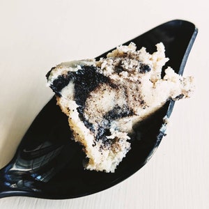 May include: A close-up of a black plastic spoon holding a scoop of black and white swirled ice cream.