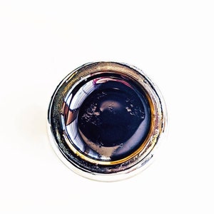 May include: Close-up of a silver bottle cap with a dark liquid inside.