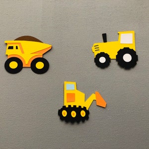 May include: Three paper cutouts of construction vehicles including a yellow dump truck with a brown load, a yellow tractor with black wheels, and a yellow excavator with a light blue window and orange arm, all featuring textured cardstock details.