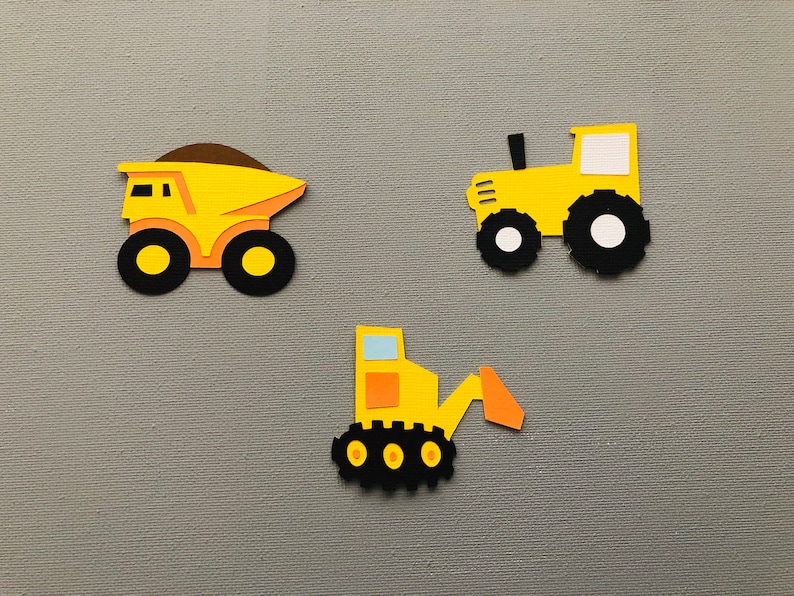 May include: Three paper cutouts of construction vehicles including a yellow dump truck with a brown load, a yellow tractor with black wheels, and a yellow excavator with a light blue window and orange arm, all featuring textured cardstock details.