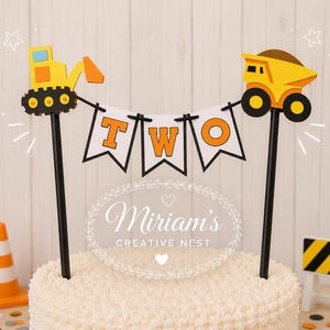 May include: A cake topper featuring a yellow excavator and a yellow dump truck connected by a white banner with the orange letters T, W, and O. The construction-themed decoration is mounted on two black sticks and includes a small orange traffic cone.