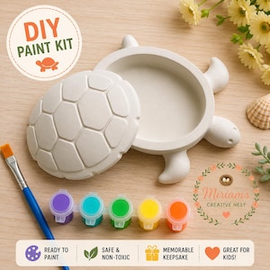 May include: A DIY paint kit featuring a white turtle-shaped trinket box with a removable shell lid, a blue-handled paintbrush, and a strip of five small paint pots in purple, teal, green, yellow, and orange. The text reads DIY PAINT KIT.