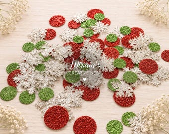 May include: A collection of glittery red, green, and silver circular confetti pieces mixed with silver snowflake-shaped confetti. The text Miriam's CREATIVE NEST is printed in white in the center of the scattered holiday-themed decorations.