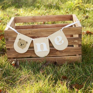 May include: A brown wooden crate with a white banner that says "one" with a bear face on the leftmost flag. The banner is hanging from the crate.