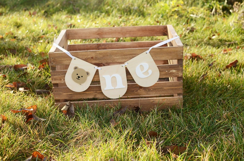 May include: A brown wooden crate with a white banner that says "one" with a bear face on the leftmost flag. The banner is hanging from the crate.