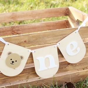 May include: A wooden crate with a white banner that says "one" in white letters. The banner has a brown bear face on one end.