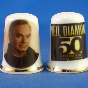 May include: Two white ceramic thimbles with gold trim. One features a portrait of a man, the other has "NEIL DIAMOND 50 YEAR ANNIVERSARY WORLD TOUR" printed on it in black and gold.