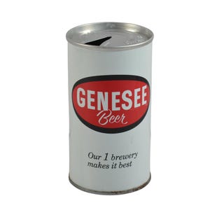 May include: A vintage Genesee Beer can with a white background and a red oval logo. The logo features the brand name in white and the word "Beer" in a cursive font. The text "Our 1 brewery makes it best" is printed below the logo.