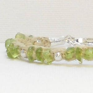 Puede incluir: Un brazalete de piedras preciosas de peridoto verde con cuentas de plata y un cordón de fibra natural.