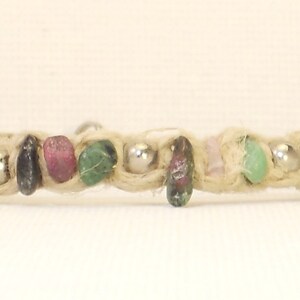 Pode incluir: Um bracelete de corda bege com contas de pedras preciosas verdes, rosa e pretas e contas espaçadoras prateadas.