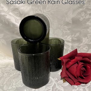 May include: Four Sasaki Green Rain Glasses with a textured surface, arranged with a red rose. The glasses are a dark olive green color. The text "Sasaki Green Rain Glasses" is at the top of the image.