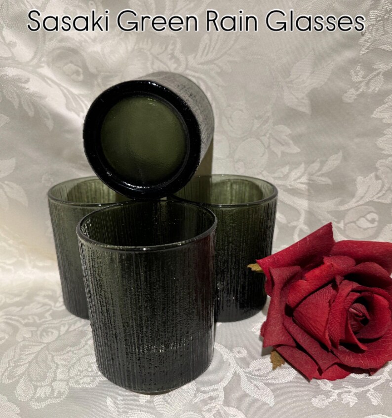 May include: Four Sasaki Green Rain Glasses with a textured surface, arranged with a red rose. The glasses are a dark olive green color. The text "Sasaki Green Rain Glasses" is at the top of the image.