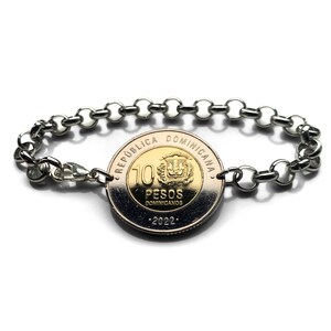 Könnte beinhalten: Ein silberfarbenes Metallkettenarmband mit einer 10-Pesos-Münze aus der Dominikanischen Republik von 2022 in der Mitte. Die Münze hat einen goldfarbenen Kern und einen silberfarbenen Außenring mit der Aufschrift REPUBLICA DOMINICANA, 10 PESOS DOMINICANOS, 2022.