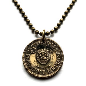 May include: A gold-toned necklace with a 5 Piastres coin pendant featuring a lion head and the text "REPUBLIQUE LIBANAISE 1961".