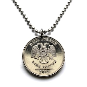 May include: A silver-colored coin pendant necklace. The coin features a double-headed eagle emblem and Cyrillic text. The necklace has a ball chain and a clasp. The coin is dated 2015.