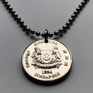 May include: A silver coin pendant necklace. The pendant is a Singapore coin from 1996, featuring a coat of arms and the word "Singapore". The necklace has a dark grey ball chain.