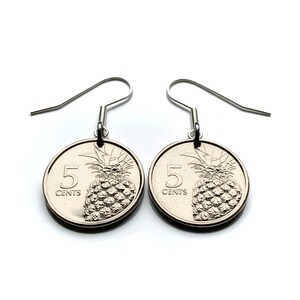Puede incluir: Un par de pendientes plateados. Cada pendiente presenta un diseño de moneda circular con una piña y el texto "5 CENTS". Los pendientes tienen un cierre de gancho.