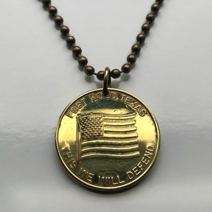 May include: A gold-toned necklace with a round pendant featuring an American flag and the text "FORT HOOD, TEXAS THIS WE WILL DEFEND".