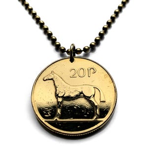 May include: A gold-colored coin pendant necklace. The pendant is a 20p coin featuring a horse illustration. The necklace has a ball chain in a matching gold tone. The coin is circular and has the number "20P" printed on it.