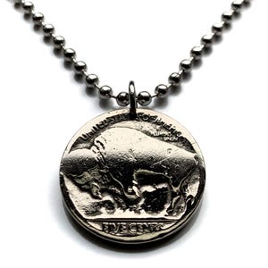May include: A silver-colored necklace featuring a pendant made from a United States nickel. The nickel pendant displays a detailed image of a bison and the words "FIVE CENTS". The necklace chain is made of small, round beads.