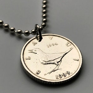 Puede incluir: Colgante de moneda plateada con diseño de pájaro, sujeto a un collar de cadena de bolas. La moneda muestra los años 1994 y 1999. Una pieza de joyería única.