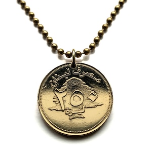 May include: A gold necklace with a round pendant featuring a Lebanese 150 Lira coin. The coin has an image of a cedar tree and the Arabic text "جمهورية لبنان" (Republic of Lebanon).