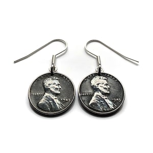 Op de afbeelding: Een paar zilverkleurige oorbellen met vintage 1943 centen. Elke cent toont een profiel van een man en de woorden "Liberty" en "In God We Trust". De oorbellen hebben eenvoudige, gebogen oorhaken.