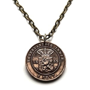 Puede incluir: Un collar de bronce con un colgante de moneda de 1 centavo de las Indias Orientales Holandesas. La moneda presenta una corona, un escudo de armas y el texto "NEDERLANDSCH INDIE 1859 1 CENT".