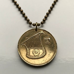 May include: A gold necklace with a round pendant featuring a lyre, a traditional musical instrument, and the Star of David. The pendant is attached to a chain with small, round beads.