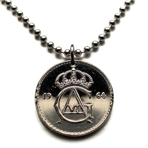 May include: A silver-toned circular coin pendant necklace featuring a ball chain. The coin displays a crown emblem above the intertwined letters AG, with the numbers 19 and 64 positioned on the left and right sides of the central design.