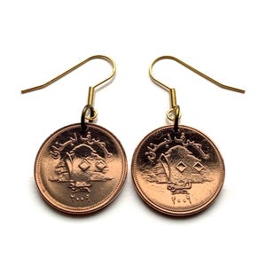 May include: A pair of gold dangle earrings featuring copper-colored coins with the Lebanese cedar tree and Arabic text. The coins are dated "1991".