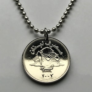 May include: A silver necklace with a silver coin pendant featuring a cedar tree and Arabic text. The coin has the year 1972 inscribed on it.