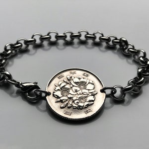 May include: A silver bracelet with a Japanese 1 yen coin charm featuring a floral design. The coin has the Japanese characters for "Japan" and "yen" on it.