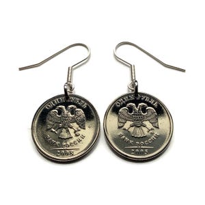 May include: Silver-toned dangle earrings featuring Russian coins. Each coin displays a double-headed eagle emblem and Cyrillic text. The earrings have a simple hook design, perfect for everyday wear.