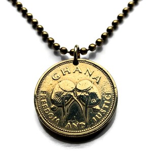 May include: A gold-colored coin pendant necklace. The coin features the word "GHANA" at the top and the words "FREEDOM AND JUSTICE" around the edge. Two stylized elephants are in the center. The necklace has a ball chain.
