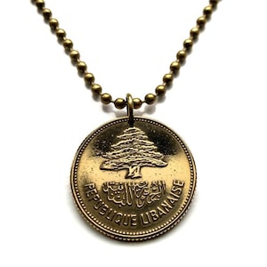 May include: A gold necklace with a round pendant featuring the Lebanese cedar tree and the text "Republique Libanaise".