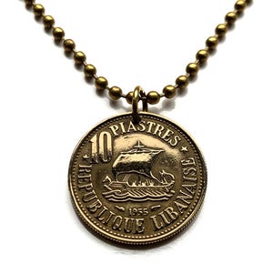 May include: A gold necklace with a 10 Piastres coin pendant featuring a ship and the text "REPUBLIQUE LIBANAISE 1955".
