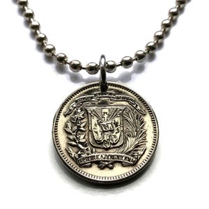 Könnte beinhalten: Silberkette mit einem silbernen Münzenanhänger, der das Wappen der Dominikanischen Republik zeigt. Die Münze trägt die Inschriften "REPUBLICA DOMINICANA" und "DIOS PATRIA LIBERTAD 1844" am Rand.