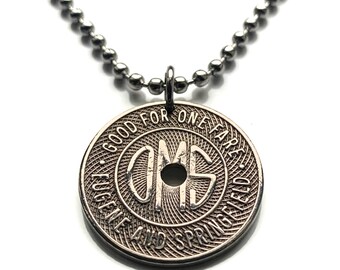 May include: A silver-toned metal coin pendant on a ball chain necklace. The circular coin features a central hole and the embossed text GOOD FOR ONE FARE and EUGENE AND SPRINGFIELD surrounding the letters OMS in a stylized, decorative font.