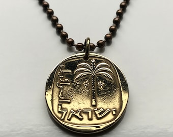 Puede incluir: Un collar de oro con un colgante redondo que presenta una palmera y texto en hebreo. El colgante está unido a una cadena marrón.