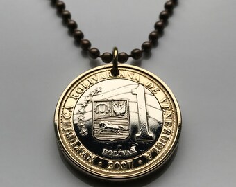 May include: A gold-toned coin pendant necklace. The coin features the text "REPUBLICA BOLIVARIANA DE VENEZUELA" and "BOLIVAR 2007". The pendant is attached to a dark brown ball chain necklace.