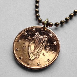 May include: A copper-colored Irish 1 cent coin with the harp of Ireland and the year 2002 on it, attached to a gold-colored chain.