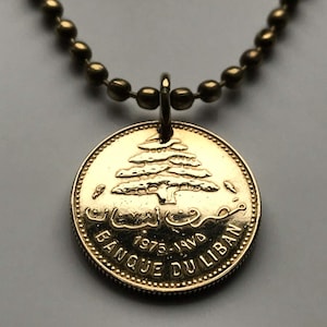 May include: Gold-colored necklace with a pendant featuring a 1975 Lebanese coin. The coin has a cedar tree and Arabic text on one side and the text "BANQUE DU LIBAN" on the other side.