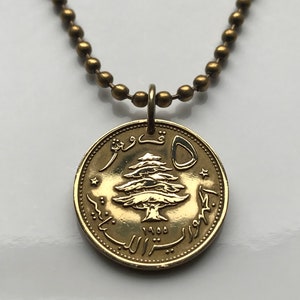 May include: A gold-colored coin pendant necklace. The coin features a detailed tree design and Arabic script. The necklace has a ball chain. The coin is approximately 1 inch in diameter.