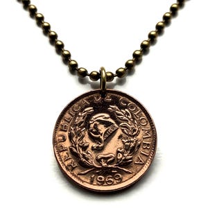 May include: A copper-colored coin pendant necklace. The coin features an emblem and the year 1969. The necklace has a bronze-colored ball chain. The pendant is round and has a detailed design.
