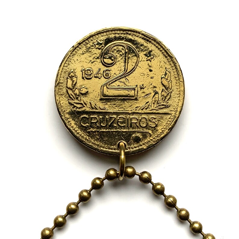 May include: A vintage gold-colored coin from 1946, featuring the number "2" and the word "CRUZEIROS". The coin is attached to a gold-tone ball chain. The coin has a worn, antique appearance.