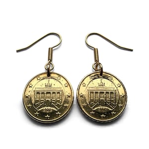 May include: A pair of gold-colored earrings featuring a coin design. Each earring displays a detailed image of a building with the year 2002. The earrings have a simple hook design for pierced ears.